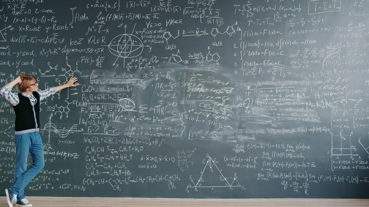 Student working through complex maths equations on a blackboard, thinking through a stuck problem